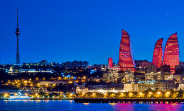 A dramatic night-time panoramic view of the Baku, Azerbaijan skyline, dominated by the three flame-shaped skyscrapers, the Flame Towers, illuminated in vibrant red, and the tall TV Tower on the left.