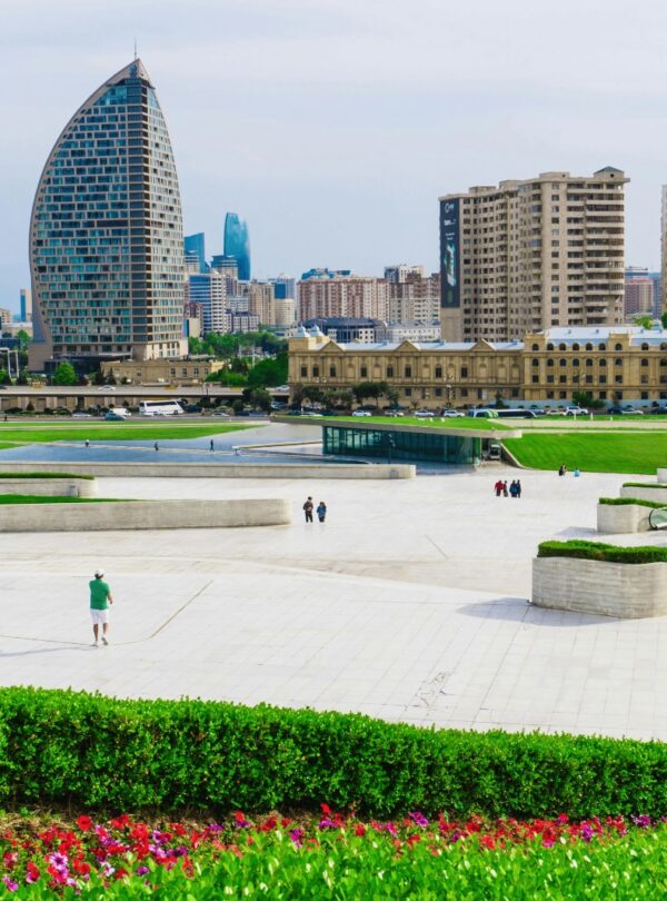 A panoramic view of the modern Baku cityscape featuring a large, bright white plaza with green landscaping and a mix of contemporary high-rise buildings, including the distinctive crescent-shaped tower.Azerbaijan 7 DAYS & 6 NIGHTS TOUR PACKAGES