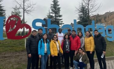 A dramatic natural gas flame burning Azerbaijan Tour Packagesstrongly in the foreground outside the stone central altar structure of the Ateshgah Fire Temple at dusk, contrasting with the dark blue sky.