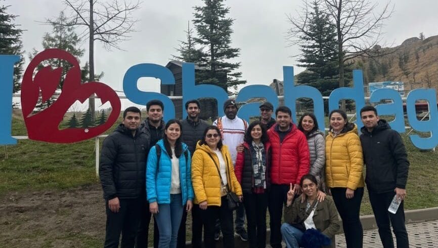 A dramatic natural gas flame burning Azerbaijan Tour Packagesstrongly in the foreground outside the stone central altar structure of the Ateshgah Fire Temple at dusk, contrasting with the dark blue sky.