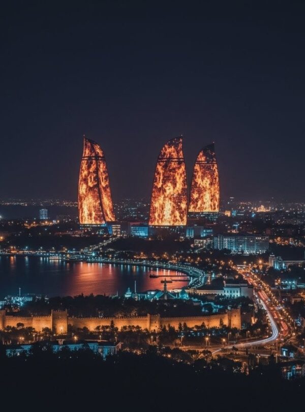 A dramatic night panoramic view of the Baku skyline featuring the tall TV Tower on the left and the three Flame Towers brilliantly illuminated in fiery red against a deep blue sky.