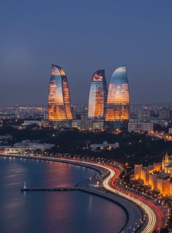 A wide-angle night view of the Baku skyline featuring the tall, illuminated Baku TV Tower on the left and the three Flame Towers brilliantly lit in vibrant red on the right, overlooking the illuminated waterfront.